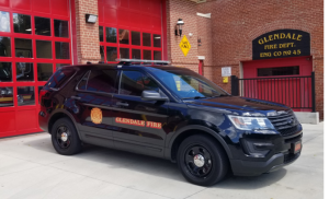 A black SUV marked "Glendale Fire" is parked in front of a red fire station with the sign "Glendale Fire Dept. Eng Co No 45." The station has large red garage doors and a brick facade. The scene is well lit, indicating it's daytime.